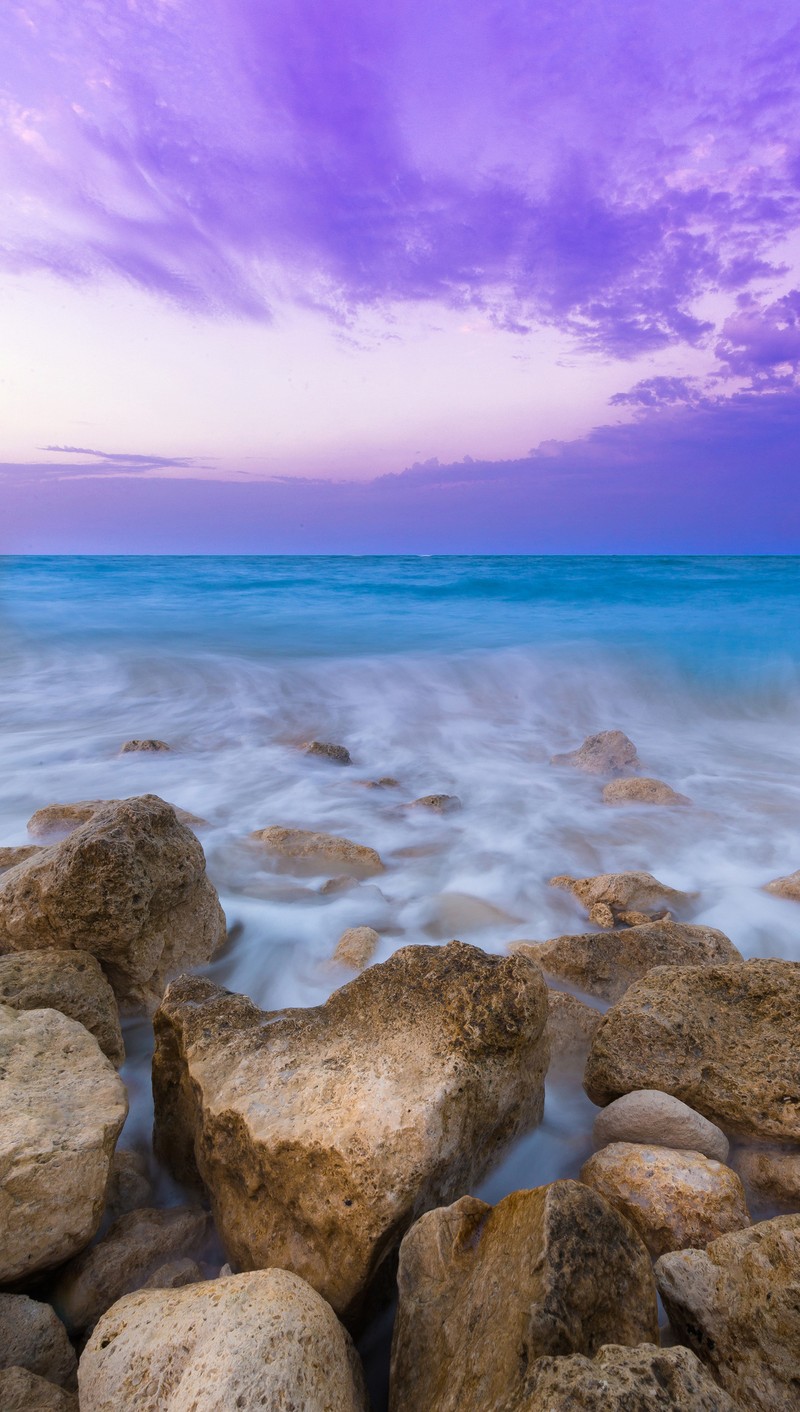 Ciel violet au-dessus de l'océan avec des rochers et de l'eau (plage, coloré, pierre)