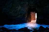 Entrada iluminada de una cueva marina entre formaciones rocosas oscuras