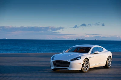 Un impresionante Aston Martin Rapide blanco estacionado contra un sereno fondo costero, mostrando su diseño elegante y características de lujo.