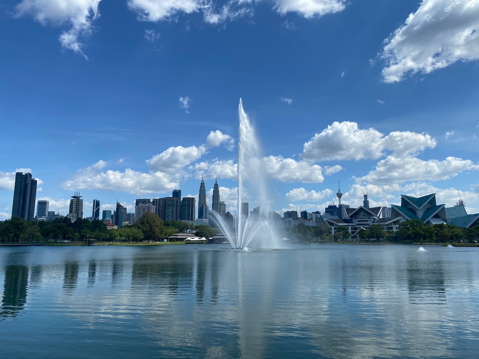 Bela fonte no meio de um lago com uma cidade ao fundo (torres petronas, kuala lumpur, cenário de montanha, recursos hídricos, água)