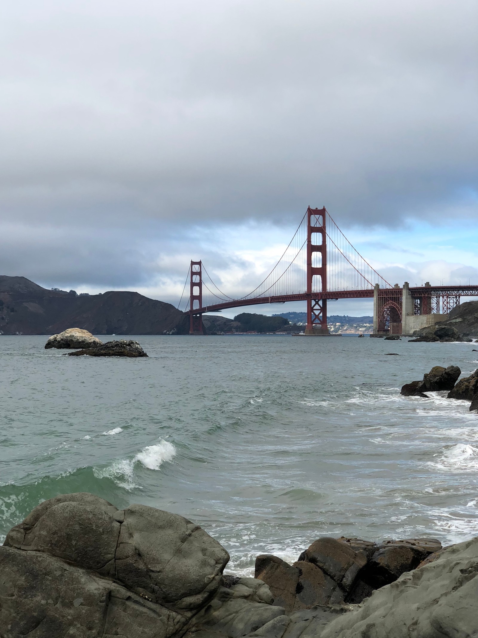 Araffe view of a bridge over a body of water with rocks in the foreground (san francisco, golden gate bridge, suspension bridge, water, baker beach)