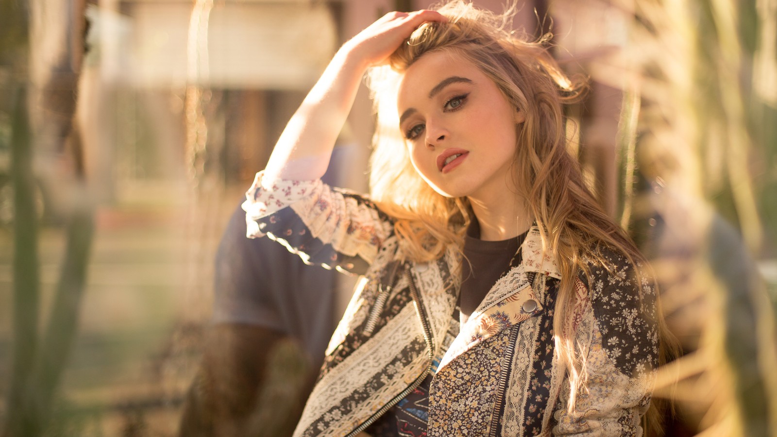 Mujer giraffe en una chaqueta floral de pie frente a un cactus (sabrina carpenter, rubia, celebridad, cantante, chicas)