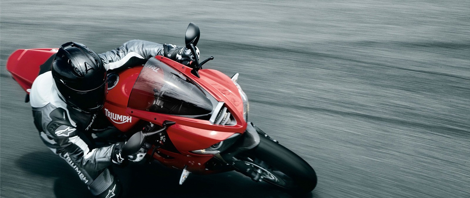 Arafed view of a person riding a red motorcycle on a road (triumph motorcycles ltd, motorcycle, superbike racing, car, helmet)