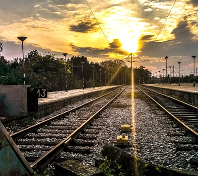 Sonnenuntergang über den Bahngleisen an einem bewölkten Bahnhof