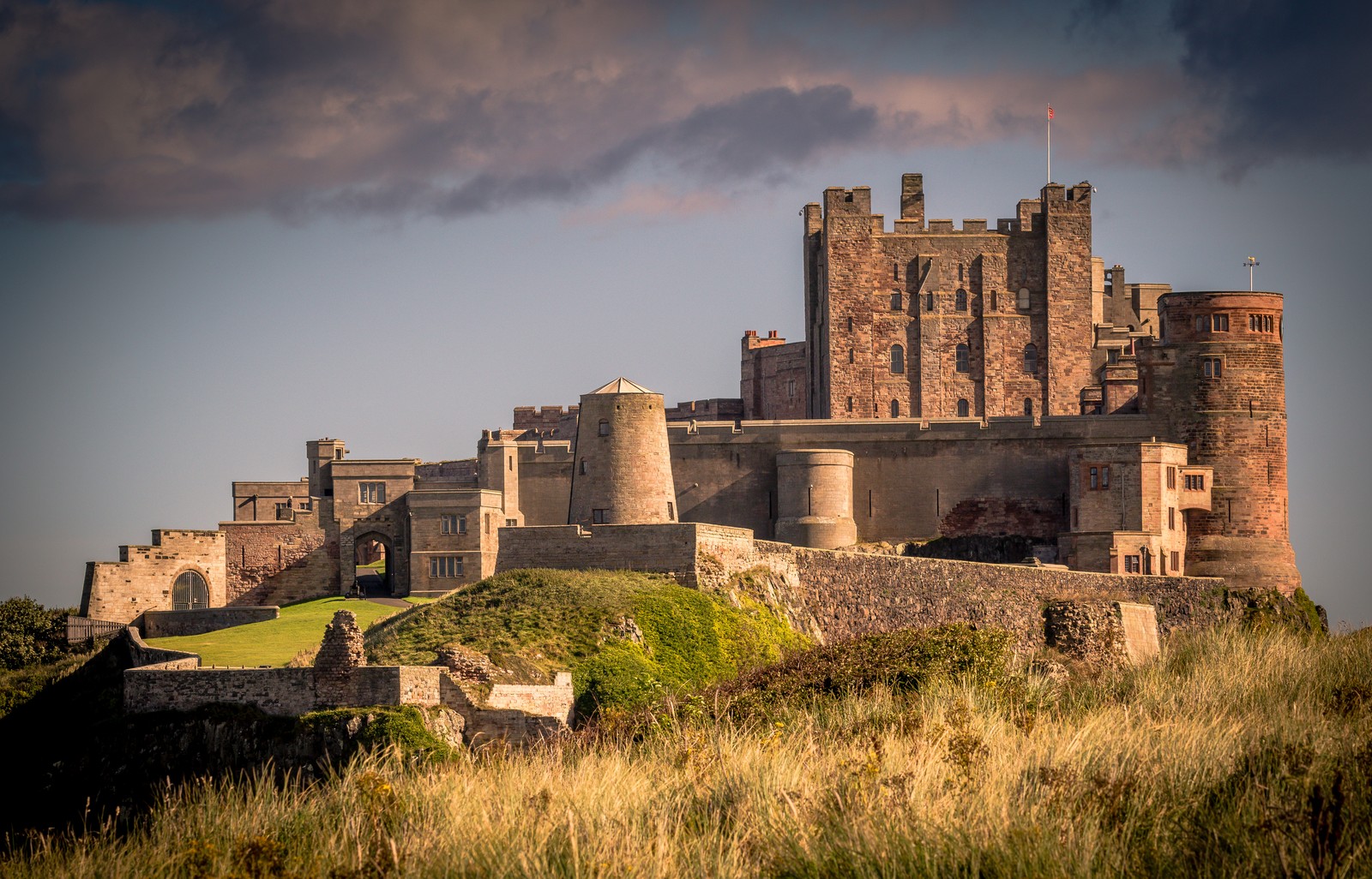 A view of a castle with a grassy field and a cloudy sky (castle, natural landscape, ruins, fortification, medieval architecture)