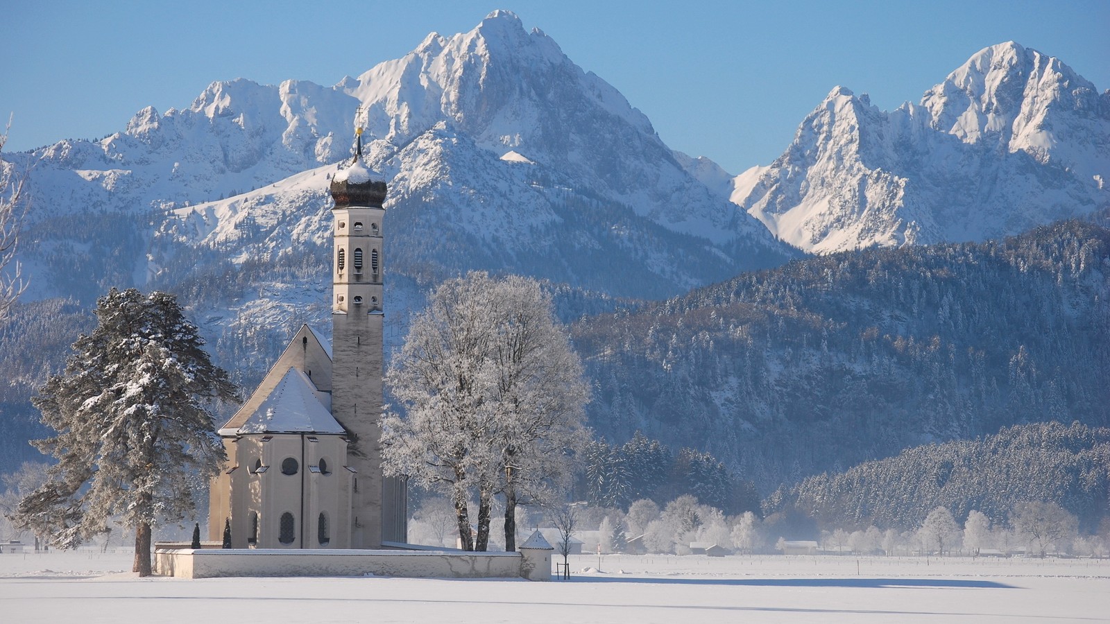 Uma paisagem nevada com uma igreja e montanhas ao fundo (formas montanhosas, montanha, inverno, cadeia de montanhas, neve)