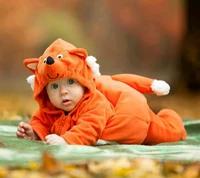 Niedliches Baby in einem gemütlichen orangefarbenen Tieroverall, das eine lebendige herbstliche Umgebung erkundet.