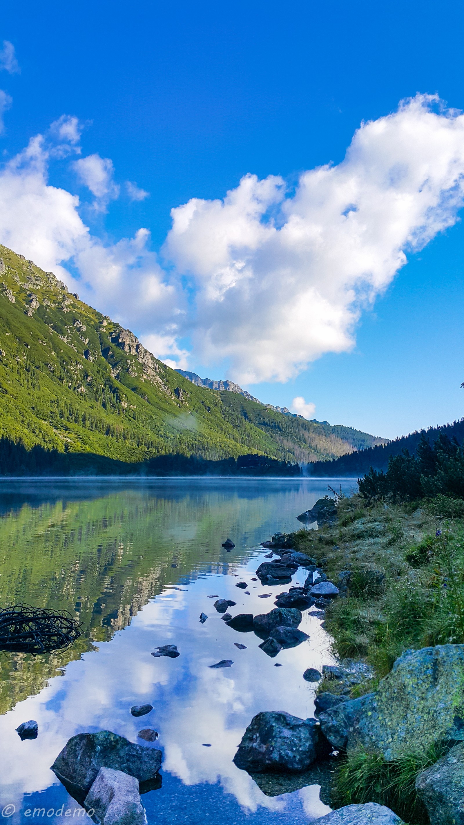 There is a lake with rocks and grass in the foreground (blue, green, lake, mountain, water)