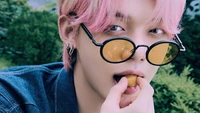 Yeonjun of Tomorrow X Together in sunglasses, playfully enjoying a snack during a vibrant photoshoot.