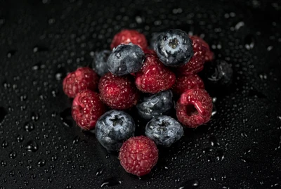 Verschiedene frische Beeren mit Tropfen auf einer dunklen Oberfläche.