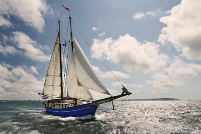 Sailing yacht gliding through shimmering waters under a partly cloudy sky.