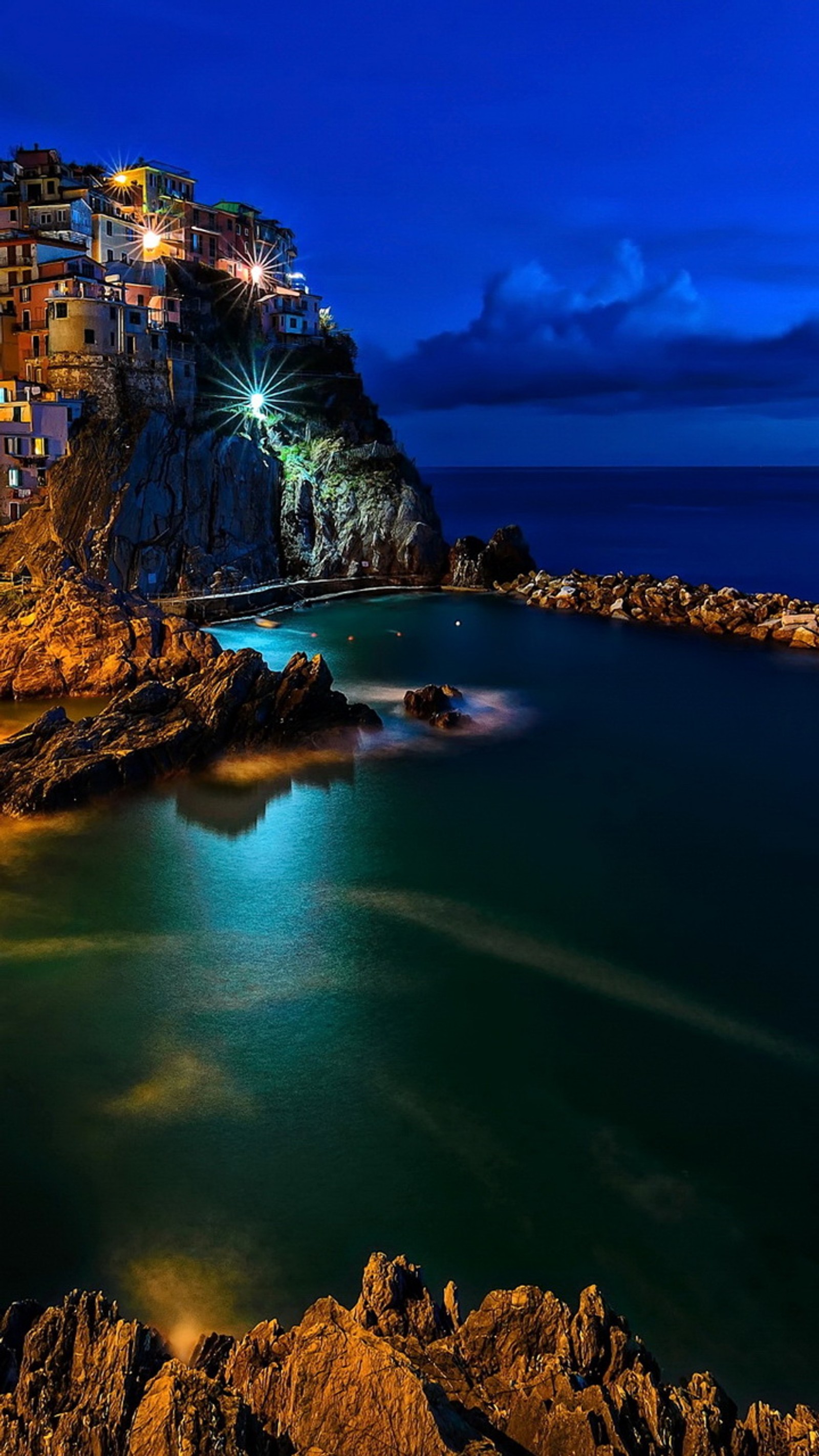 Vista nocturna de una playa con un acantilado y un cuerpo de agua (ciudad, italia, luces, noche, rocas)