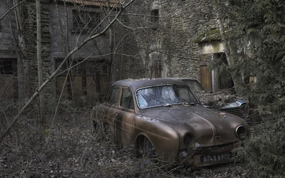 Coche vintage abandonado rodeado de vegetación crecida cerca de un edificio de piedra.