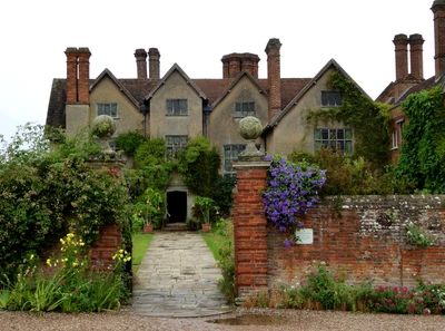 Charming manor house surrounded by lush gardens and vibrant flowers, showcasing medieval architecture and inviting pathways.