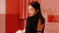 Irene de Red Velvet pose élégamment dans une tenue noire stylée devant un fond rose vif, dégageant confiance et charme.