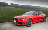 Audi RS 6 Avant in striking red, showcasing a sleek design with sporty upgrades and bold rims against a scenic backdrop.