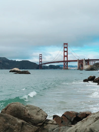 El Puente Golden Gate que se extiende sobre una bahía serena, enmarcada por costas rocosas y un cielo nublado.