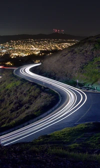 Carretera nocturna serpenteante con luces de la ciudad de fondo