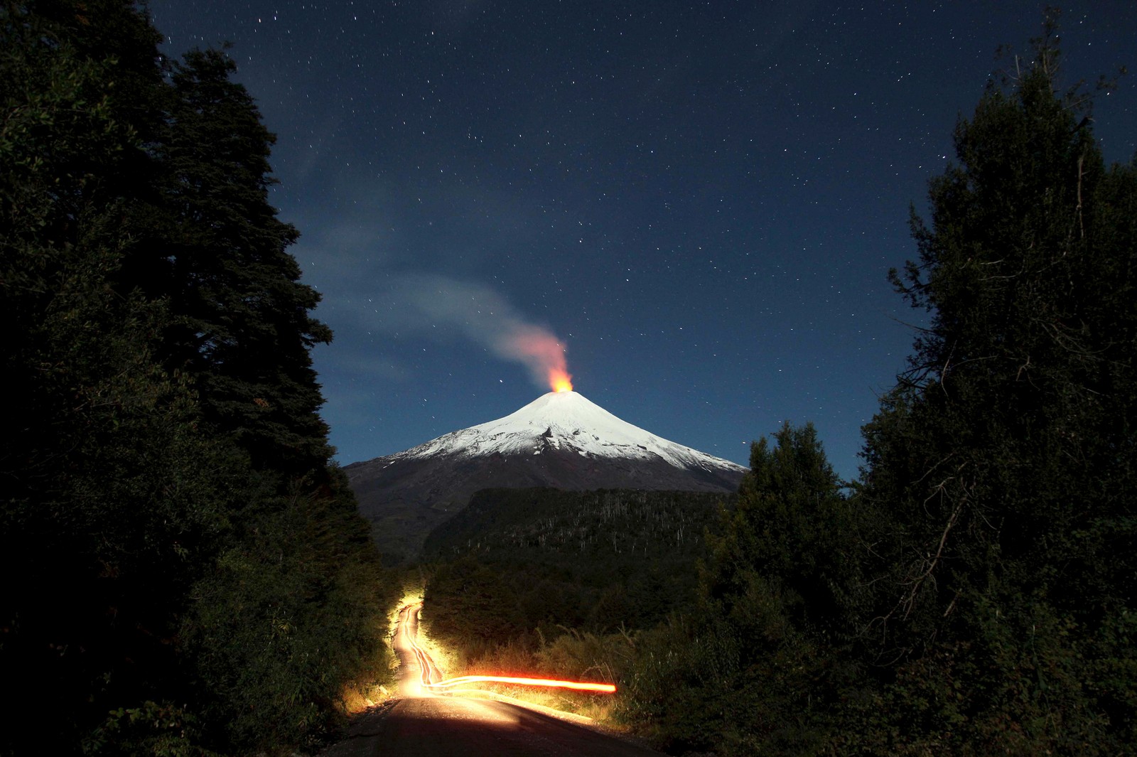 Une montagne avec une route passant à travers elle la nuit (villarrica, volcan, lac de lave, forme volcanique, types déruptions volcaniques)