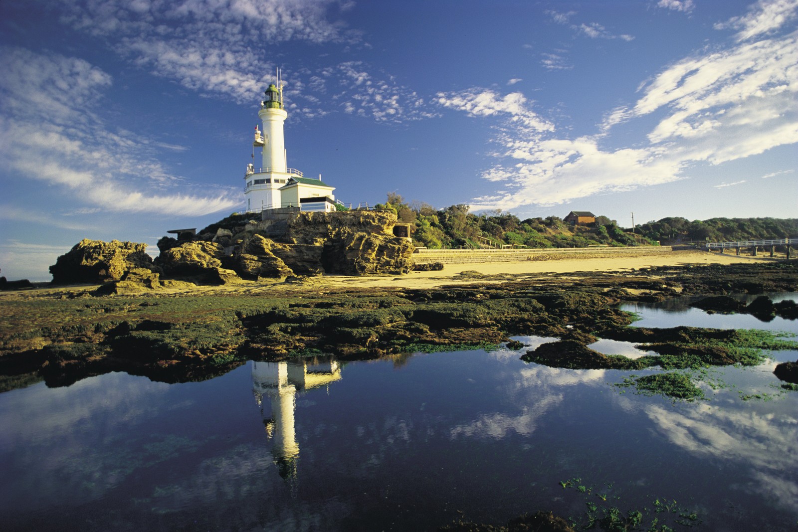 Um farol em uma costa rochosa com um céu azul (farol, reflexo, torre, recursos hídricos, costa)