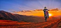 A motocross rider performing a wheelie against a stunning sunset backdrop, with mountains and a vibrant sky enhancing the thrill of extreme sport.