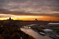 Moscow State University at sunset, casting a silhouette over the cityscape and river, with vibrant twilight colors illuminating the horizon.