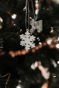 Adorno de copo de nieve plateado colgando de un árbol de Navidad, rodeado de luces cálidas y decoraciones festivas.