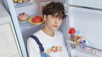 Huening Kai of Tomorrow X Together posing playfully inside a refrigerator, surrounded by colorful snacks and treats.