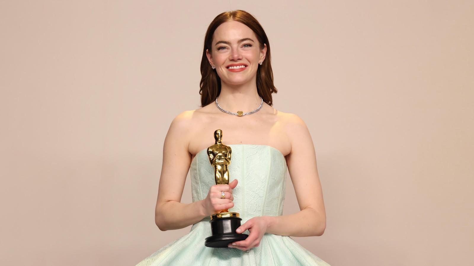 Uma mulher em um vestido segurando uma estatueta do oscar (emma stone, óscar, celebridade, troféu, atriz)