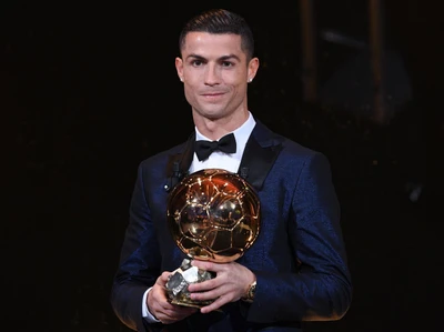 Cristiano Ronaldo segurando o troféu da Bola de Ouro, vestido com um terno formal.