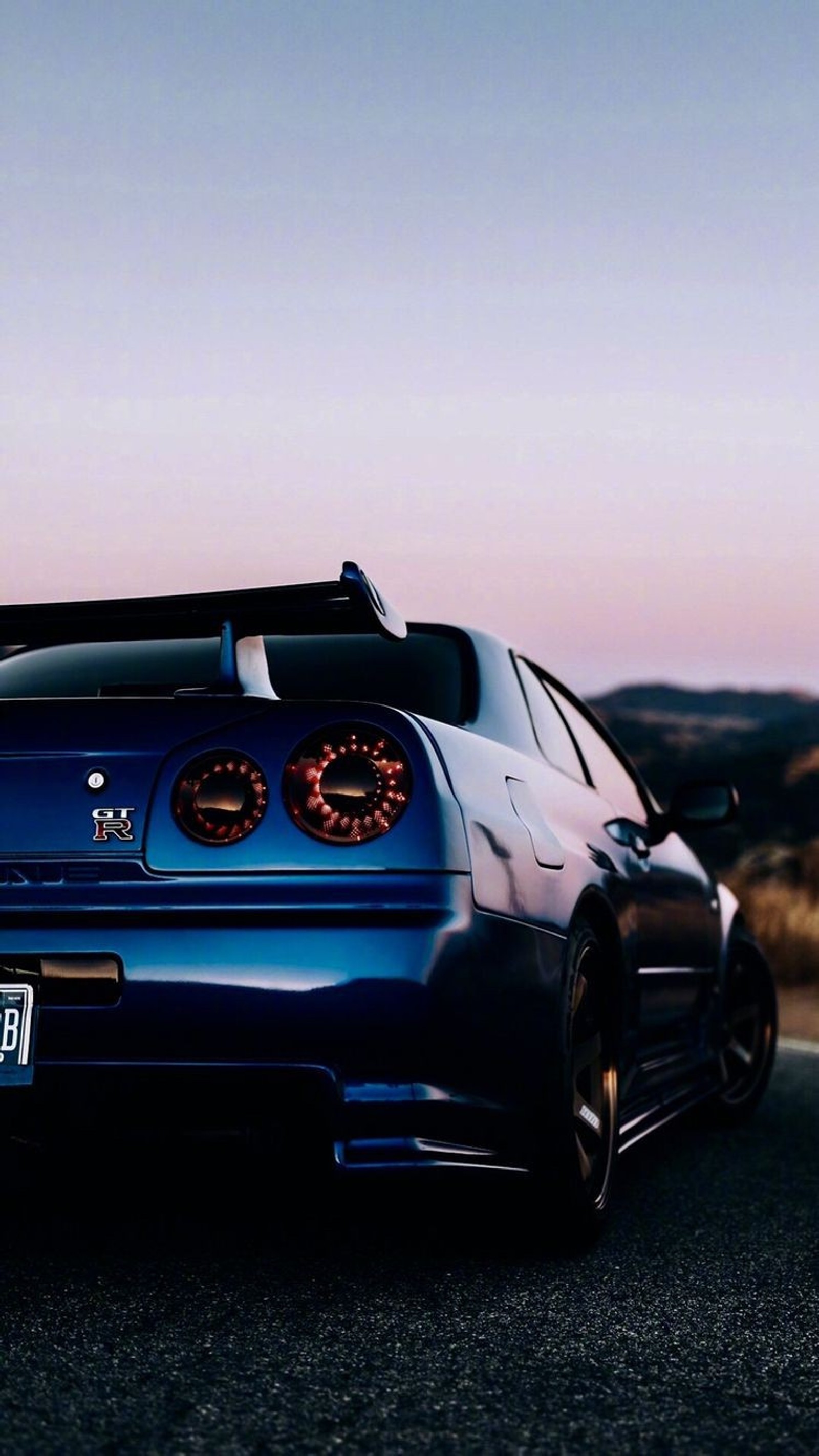 A close up of a blue car parked on a road near a mountain (hd, tuning, skyline, nissan, gtr)