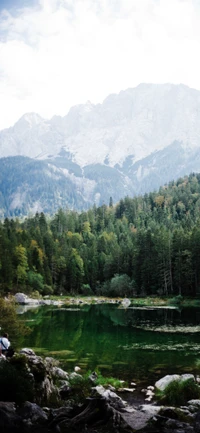 Lago de montaña sereno rodeado de un bosque exuberante y picos majestuosos