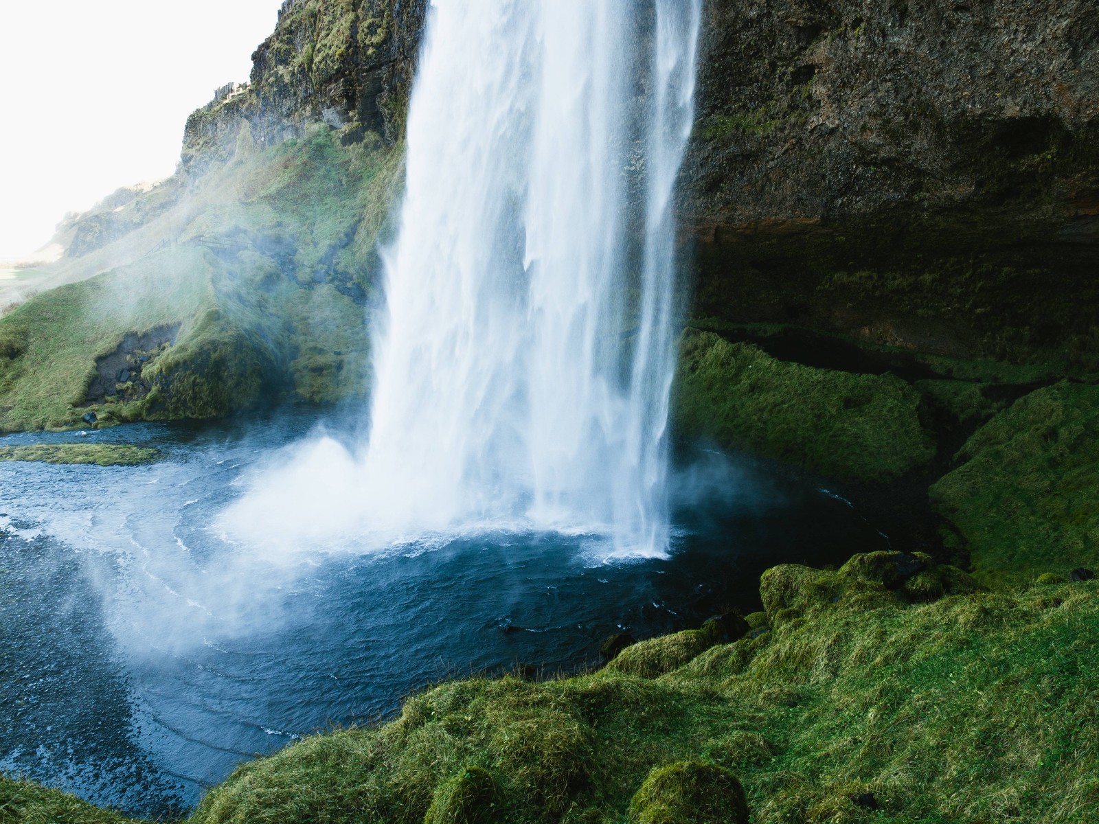 Un primer plano de una cascada con una persona de pie frente a ella (cascada, cuerpo de agua, recursos hídricos, naturaleza, agua)