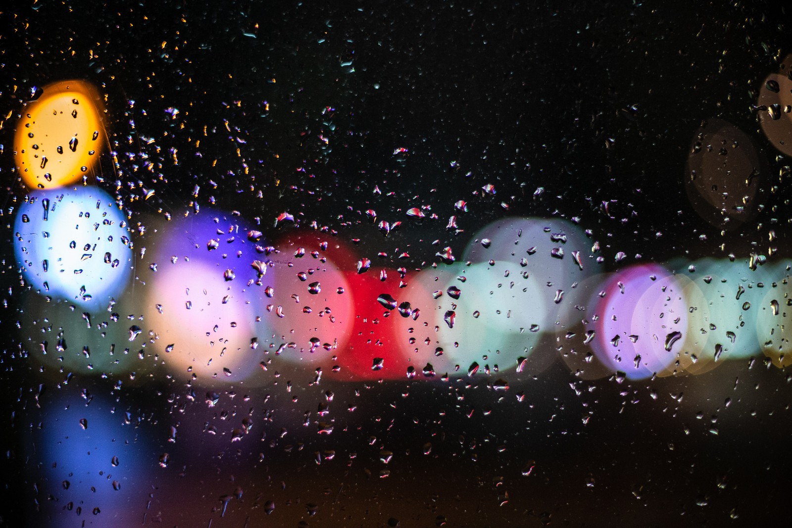 Um close de uma janela com gotas de chuva nela (brilho, bokeh, luz, água, chuva)