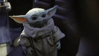 Baby Yoda in einem gemütlichen Bademantel, neugierig von seinem Platz in "The Mandalorian" blickend.