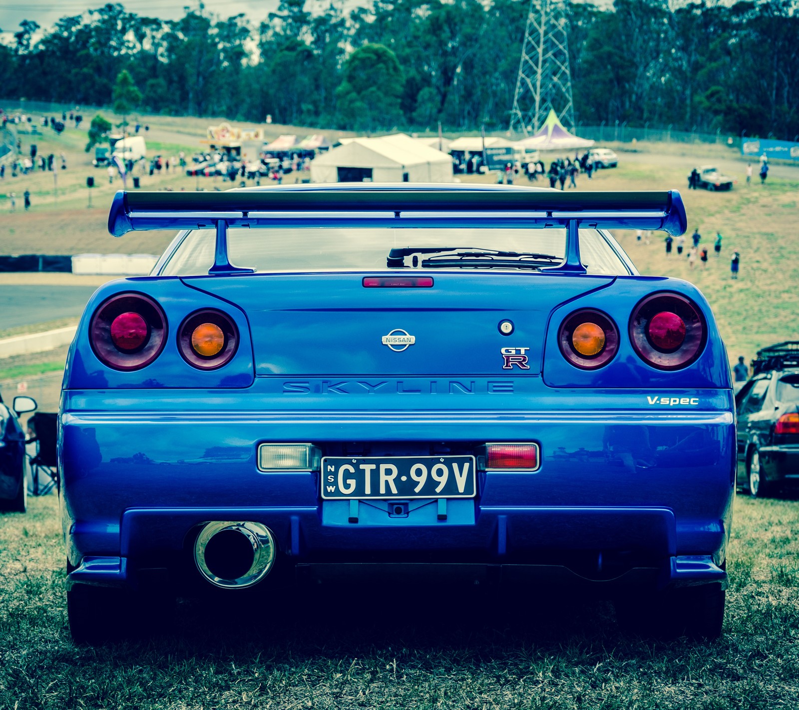 There is a blue car parked on the grass with other cars in the background (auto, car, gt r, nismo, nissan)