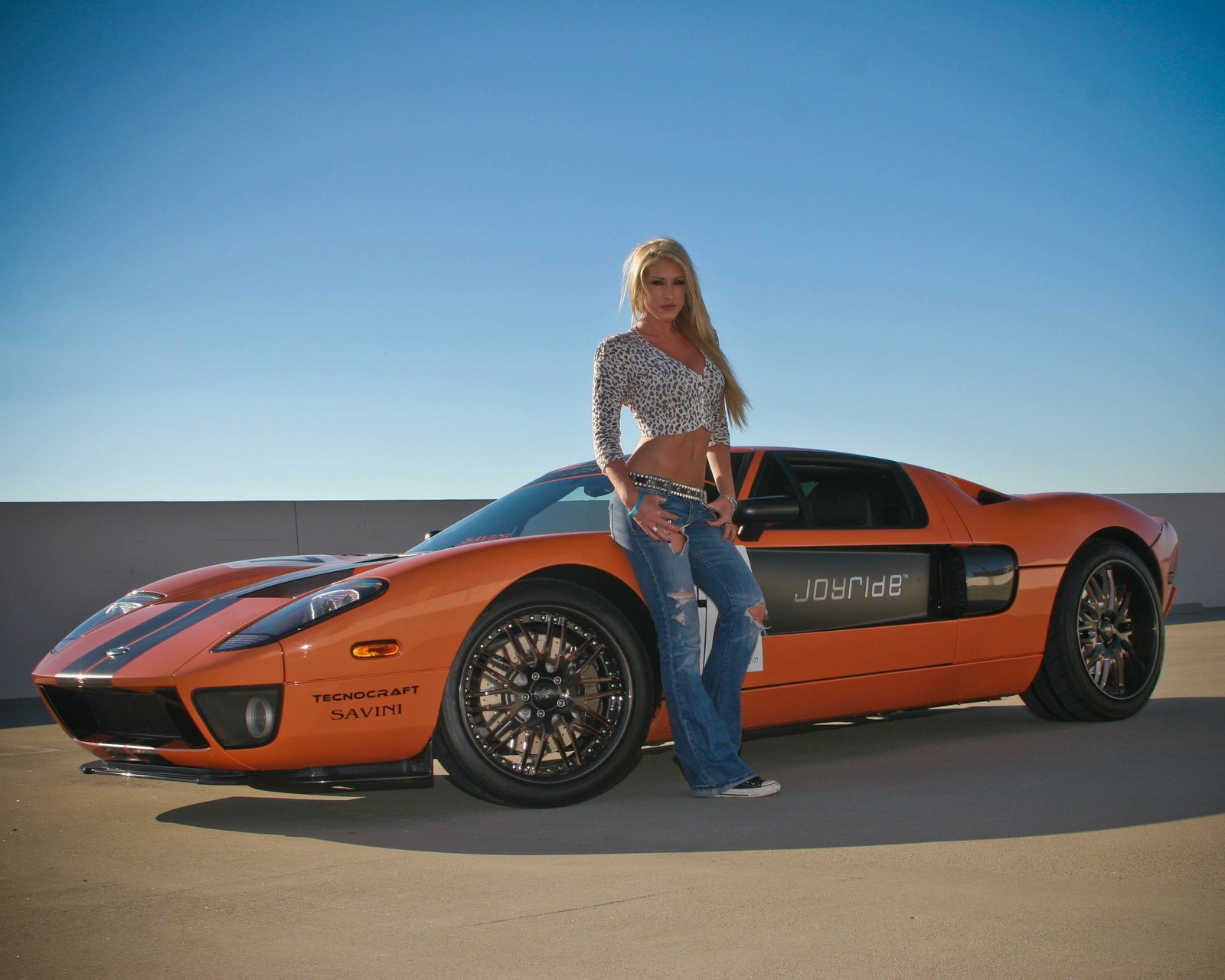 Mulher em pé ao lado de um carro esportivo com uma faixa azul e laranja (ford gt, menina)