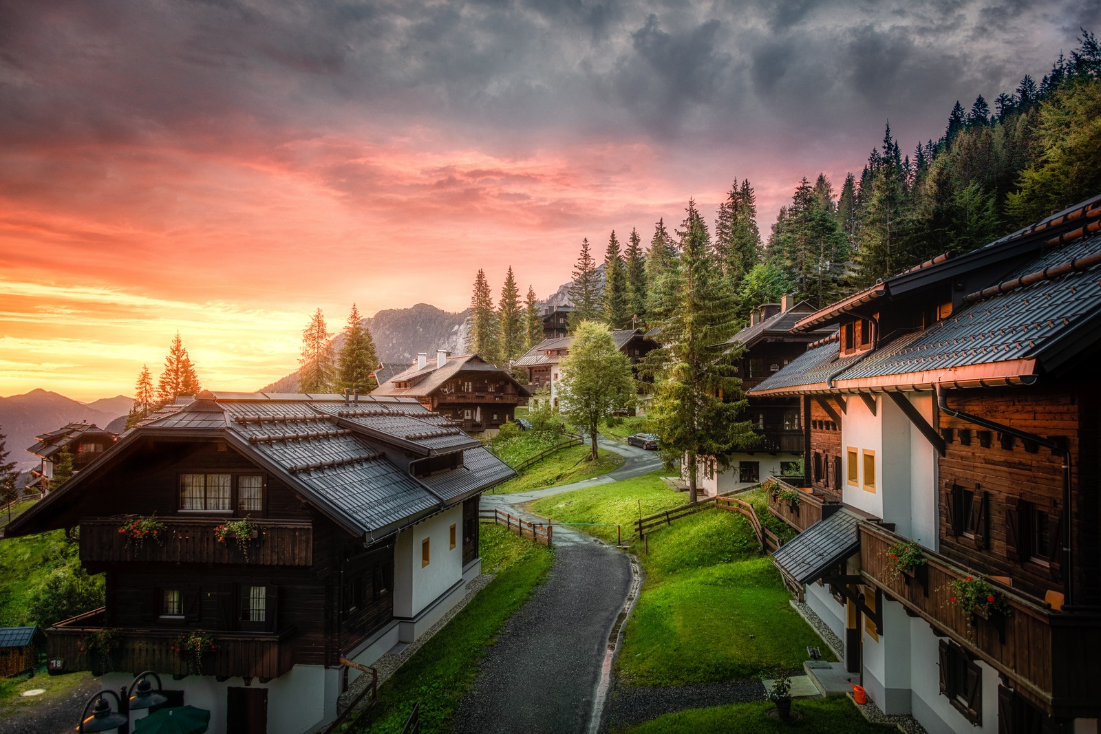 Uma vista aérea de uma aldeia com uma estrada e uma montanha ao fundo (casa de madeira, nascer do sol, paisagem, sonnleitn village, southern carinthia)