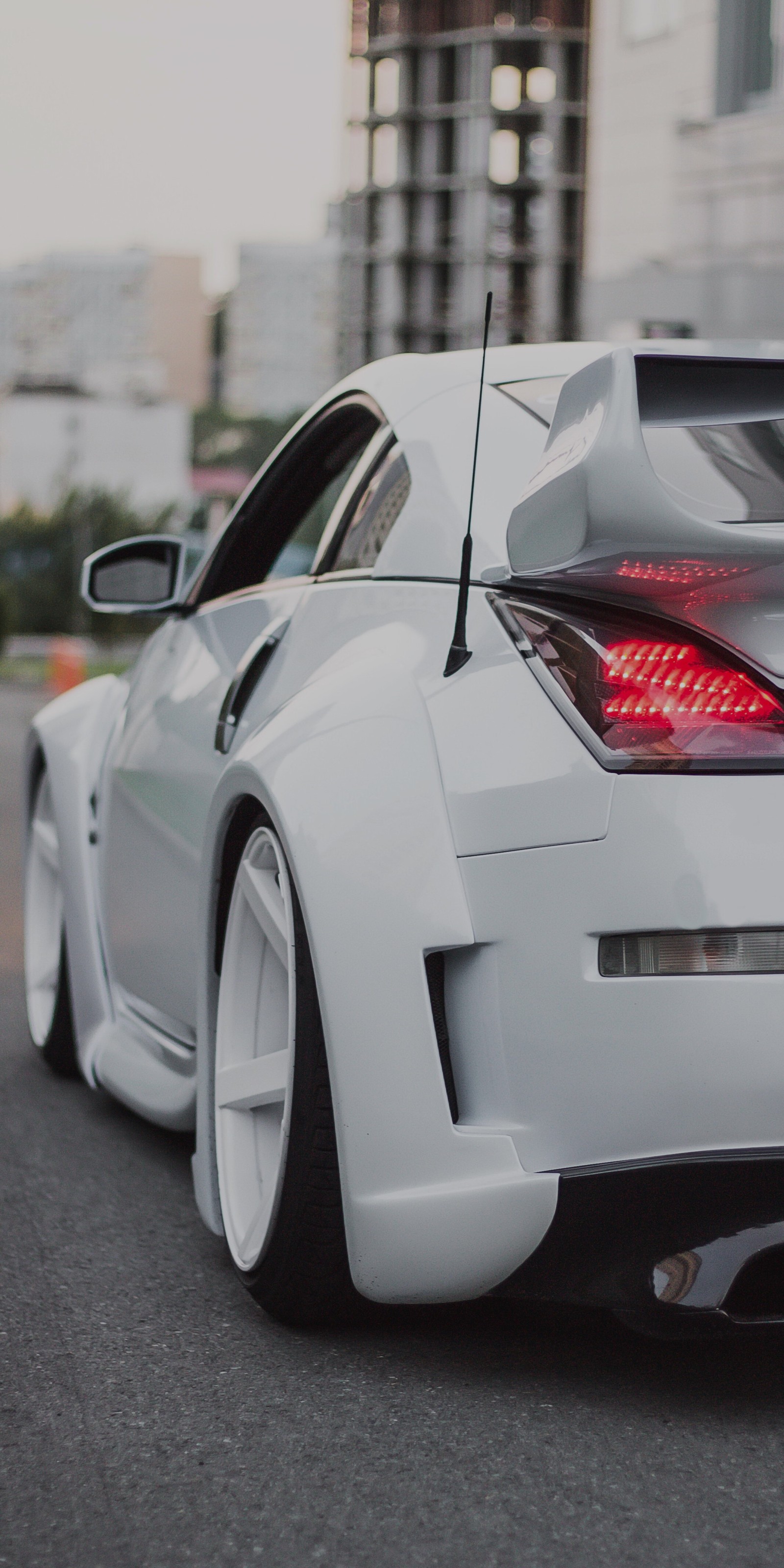 There is a white sports car parked on the street with a city in the background (cars, nissan gt r, sports car, nissan, nissan skyline gt r)