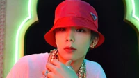 Shotaro do NCT U exibe um visual estiloso em um ambiente vibrante, adornado com acessórios e um chapéu bucket vermelho, incorporando a essência da moda K-pop.