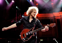 Brian May actuando enérgicamente en el escenario con su guitarra icónica, cautivando a la audiencia con su arte musical.