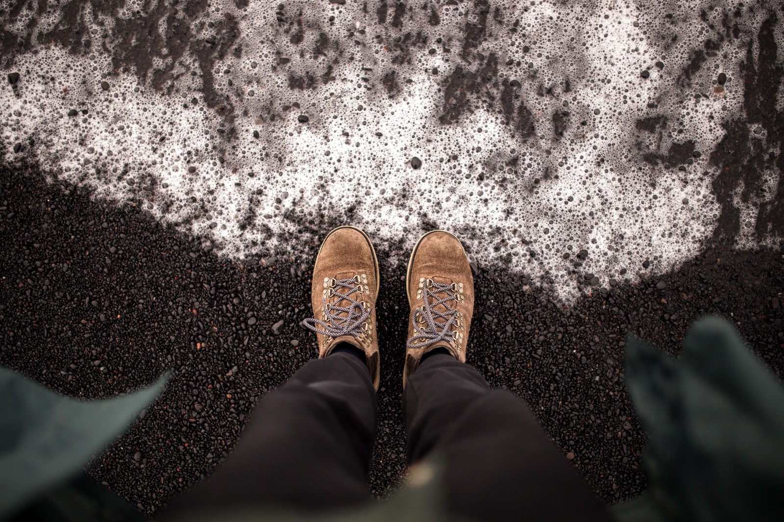 Someone standing on the ground with their feet up in front of a wave (foot, shoe, quotation, soil, leg)