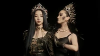 Aespa: Karina and Yoo Ji Min in a striking, regal duet, adorned with elaborate crowns and captivating black attire against a dark backdrop.