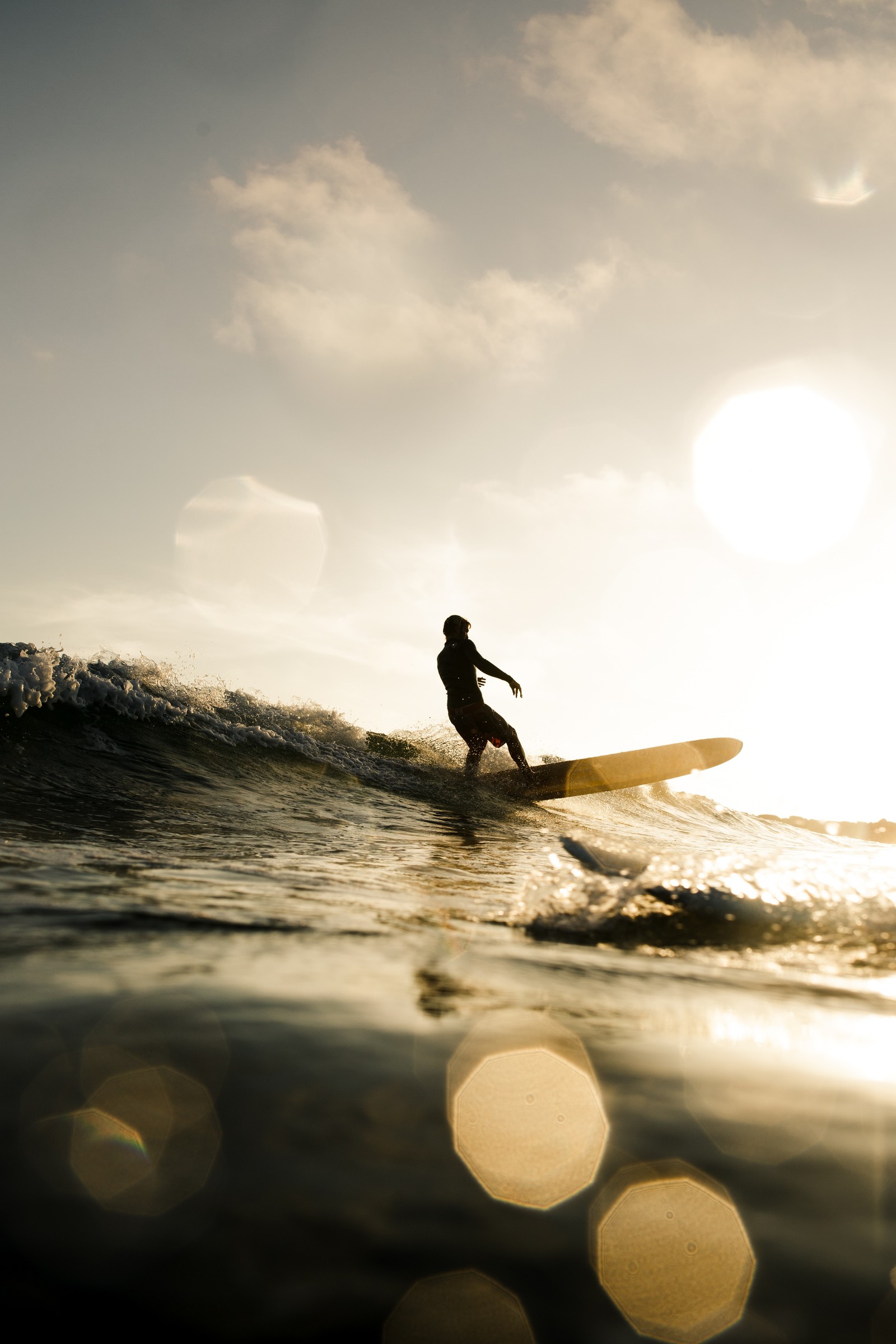 Surfer riding a wave in the ocean at sunset with sun shining (surfing, longboard, wave, surfboard, water)