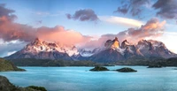 Majestic panorama of Torres del Paine National Park, featuring towering mountains under a partly cloudy sky, illuminated by the warm glow of sunset.