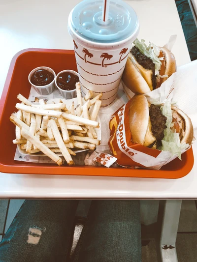 A vibrant meal featuring two burgers, golden French fries, dipping sauces, and a drink, served on a red tray.