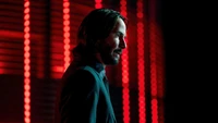 Keanu Reeves as John Wick in a dramatic silhouette against a backdrop of red lights.