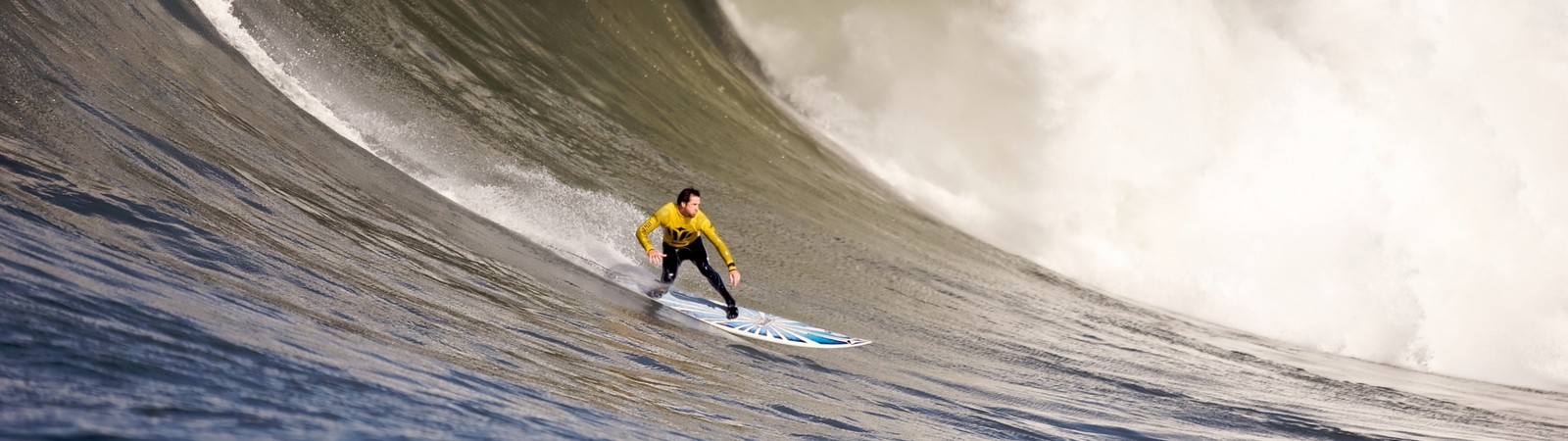 Surfer in yellow shirt riding a wave on a blue surfboard (surfing, big wave surfing, surfboard, extreme sport, boardsport)