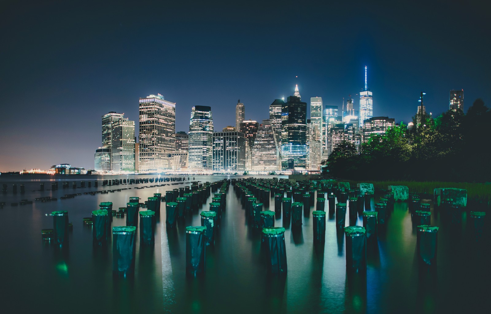 Blick auf die skyline einer stadt bei nacht mit einem pier im vordergrund (new york city, manhattan skyline, skyline, nacht, beleuchtet)