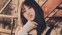 Hirai Momo do TWICE posa elegantemente, sinalizando de forma brincalhona por silêncio com o dedo nos lábios, contra um fundo de texturas rústicas.